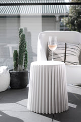 White ribbed Tom stool used as a side table on a sunny patio beside a cactus and modern chair.