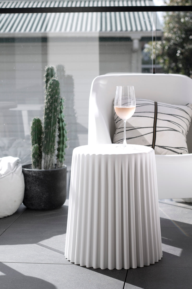 White ribbed Tom stool used as a side table on a sunny patio beside a cactus and modern chair.