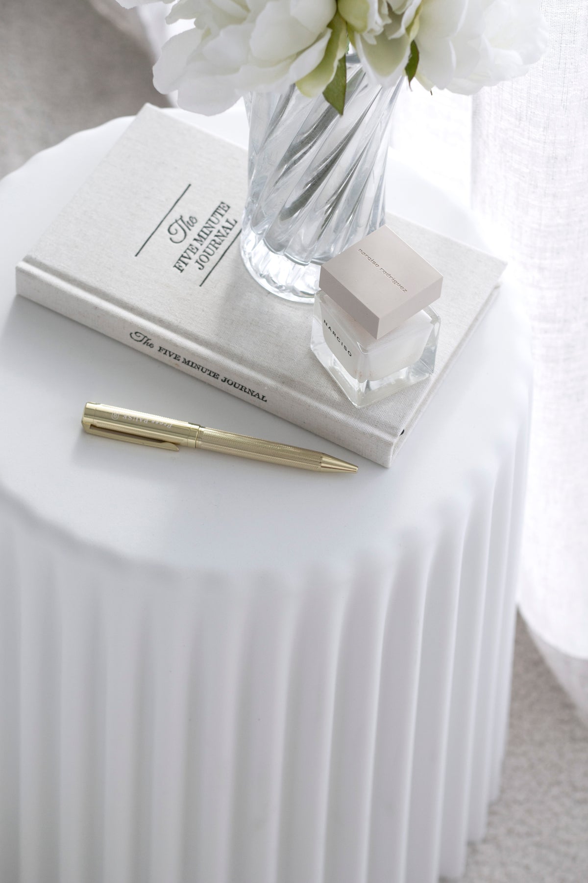 White ribbed Tom Stool styled as a side table with flowers, journal, pen, and candle – minimal coastal look