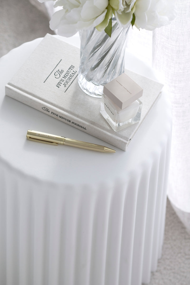 White ribbed Tom Stool styled as a side table with flowers, journal, pen, and candle – minimal coastal look