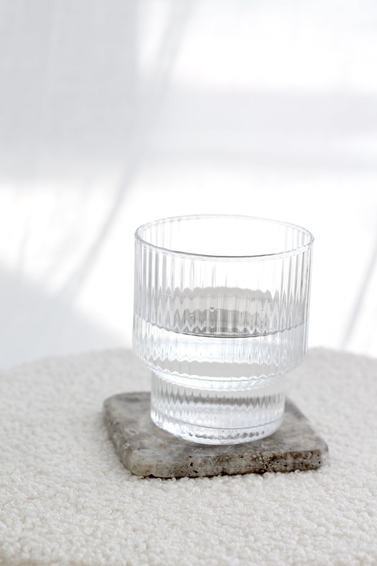 Set of 4 travertine and dark marble stone coasters with natural veining, styled with glassware on a soft textured surface