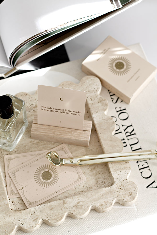 Close-up of travertine scalloped tray styled with cards, perfume, and accessories on a coffee table, showcasing natural stone texture and wavy edges.