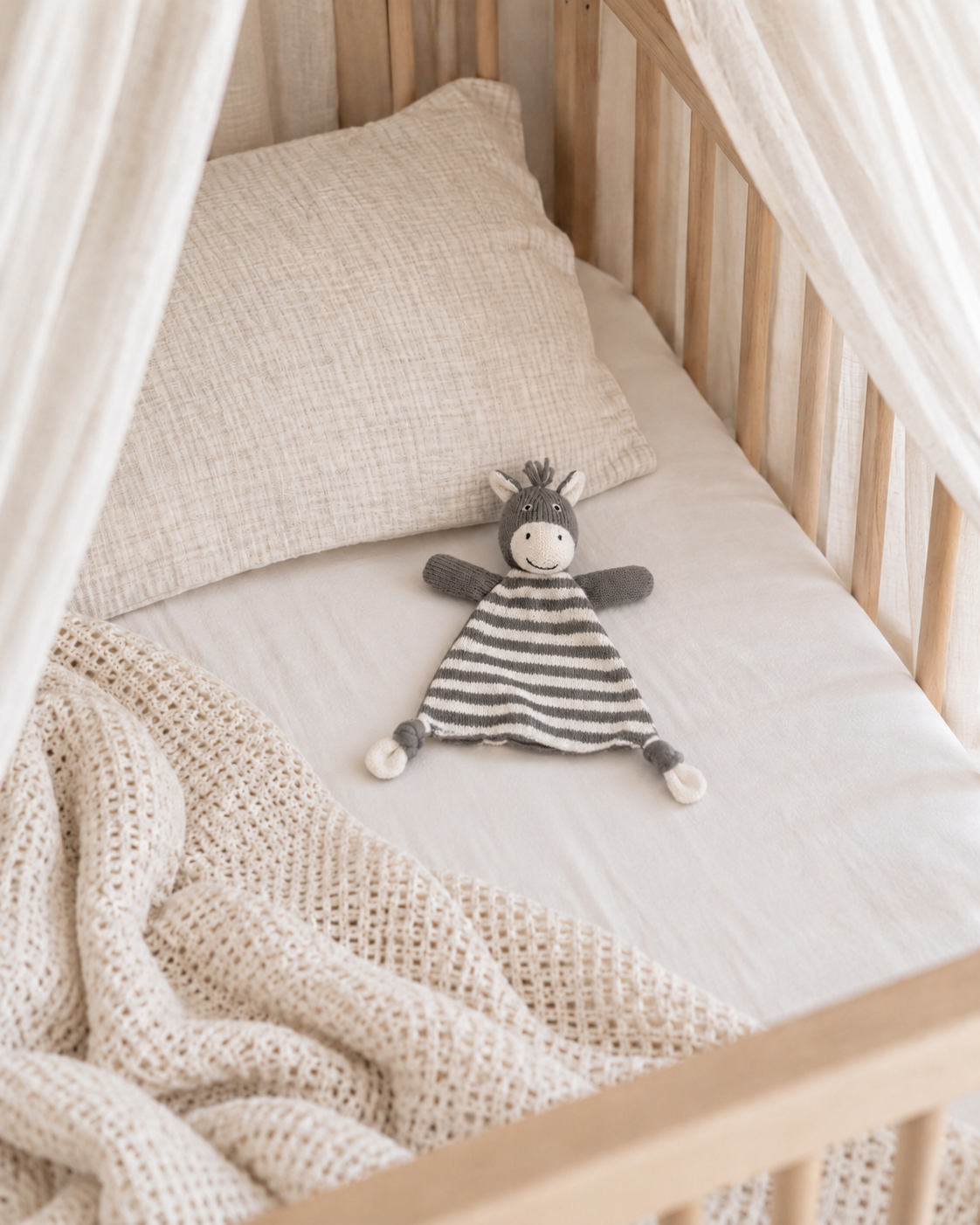 Bowie the zebra knitted comforter on a white sheet in a timber canopy cot with a waffle blanket