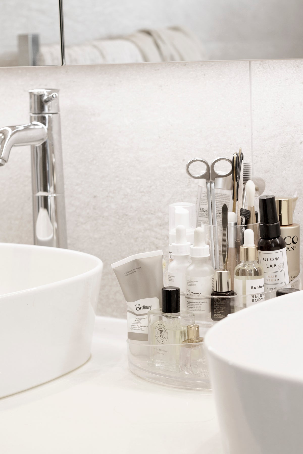 Umbra Cascada clear rotating organiser on a vanity between two white basins
