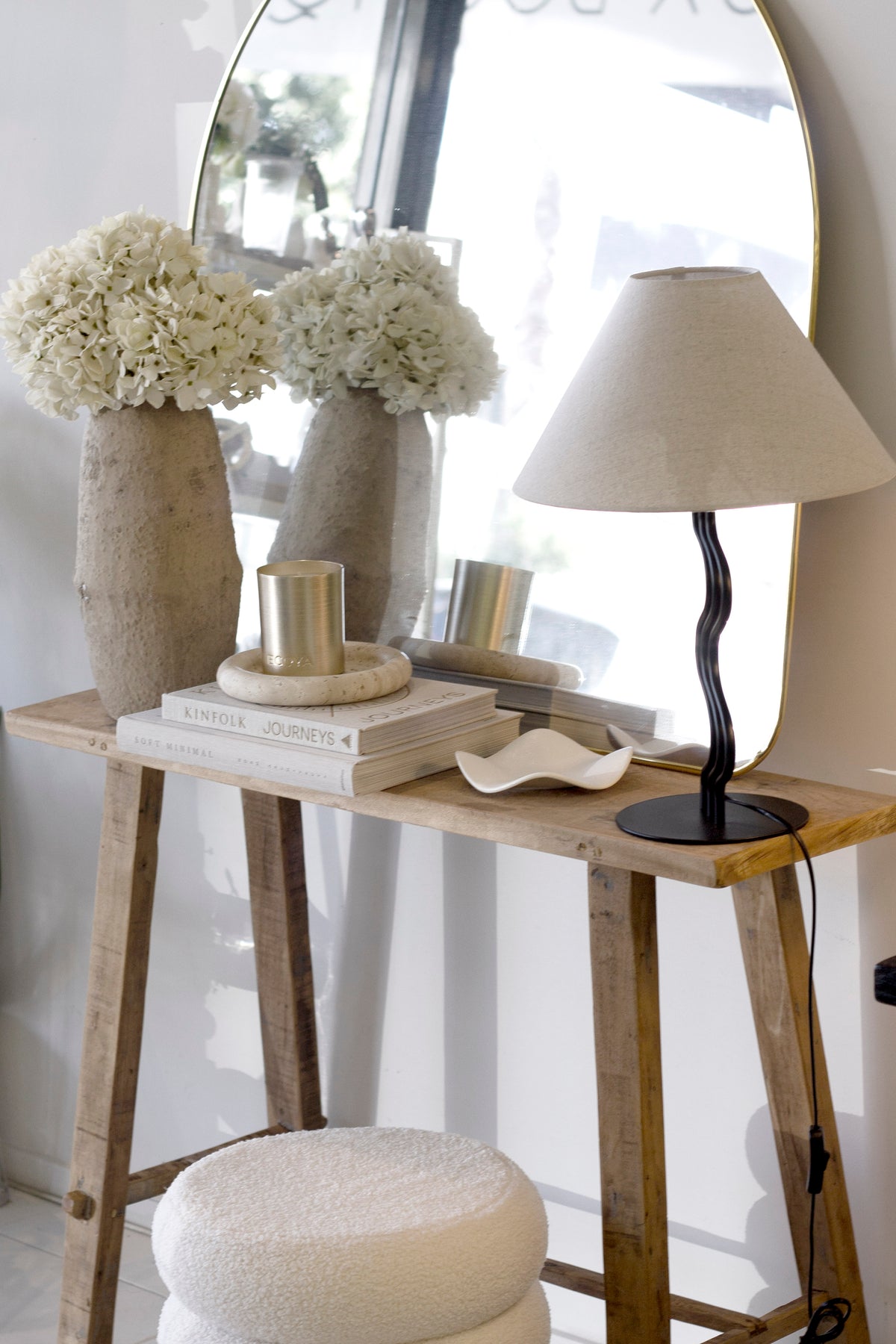 Large Umbra Hubba Arched Mirror with brass frame styled on a rustic console with flowers and lamp, modern entryway decor.