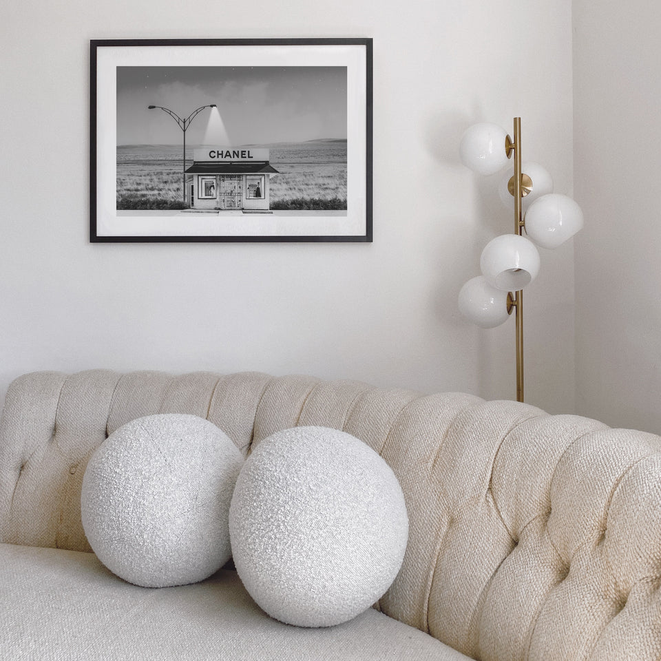 Chanel Shop print in a black frame above a tufted beige sofa with round boucle cushions and a globe floor lamp