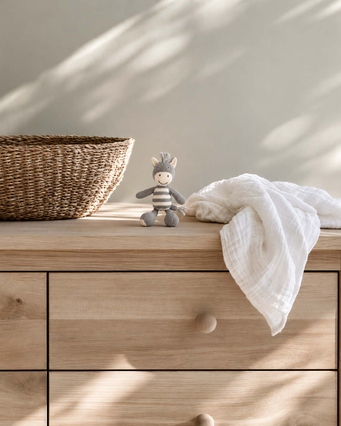 Bowie the zebra knitted rattle on an oak chest of drawers beside a woven basket and white muslin