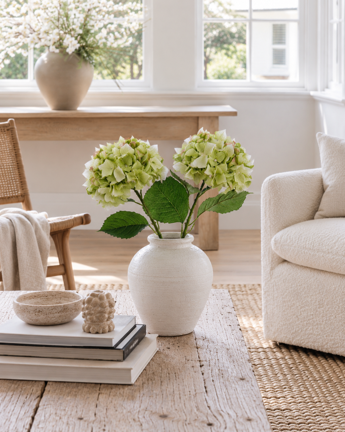 Two green faux hydrangea stems in a white vase on a rustic coffee table