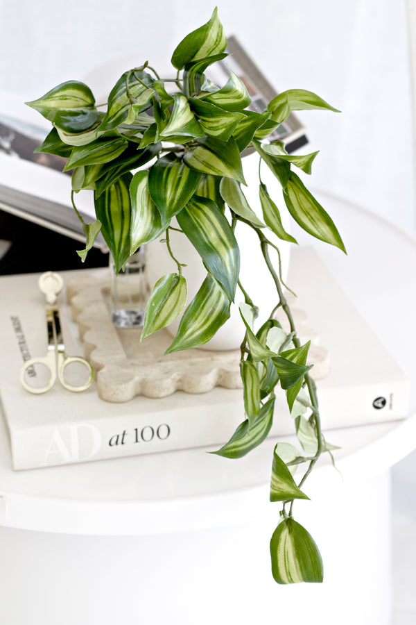 Artificial trailing greenery styled on a side table – Vanilla Orchid Leaf Bush 46cm with realistic soft green leaves draping over books.