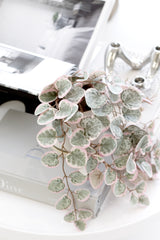 Faux variegated string of hearts trailing plant with pink and green heart-shaped leaves styled on books.
