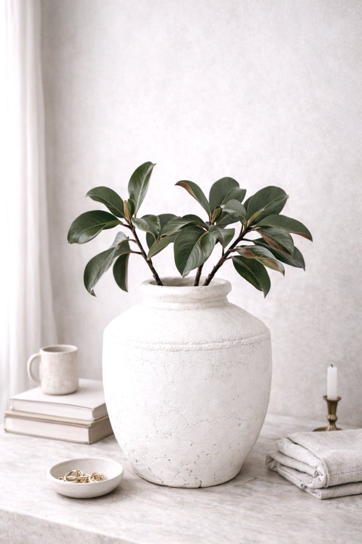 Rafaela vase holding a magnolia leaf spray on a marble ledge with folded linens and a slim candle