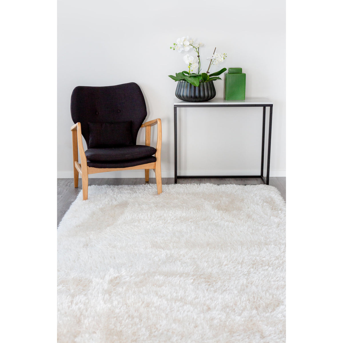 White shag rug in a bright room with a black armchair and a slim console holding a plant