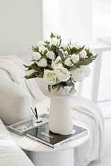 White vintage peony faux stems arranged in ceramic vase on bedside table
