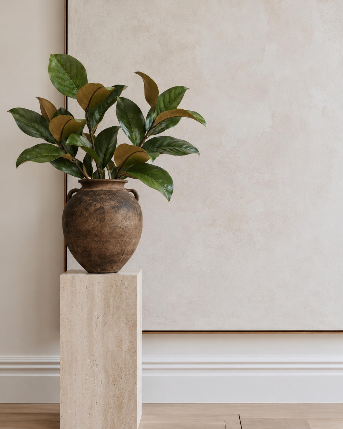 Faux magnolia leaf sprays in an aged clay urn on a travertine plinth against a pale wall