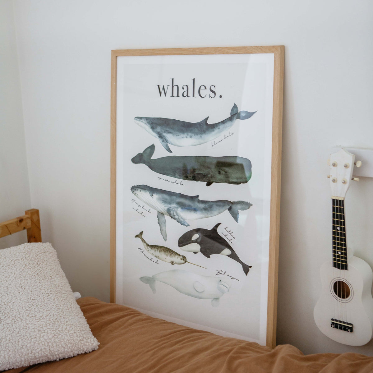 Watercolour Whales print in a natural frame on a bed beside a ukulele