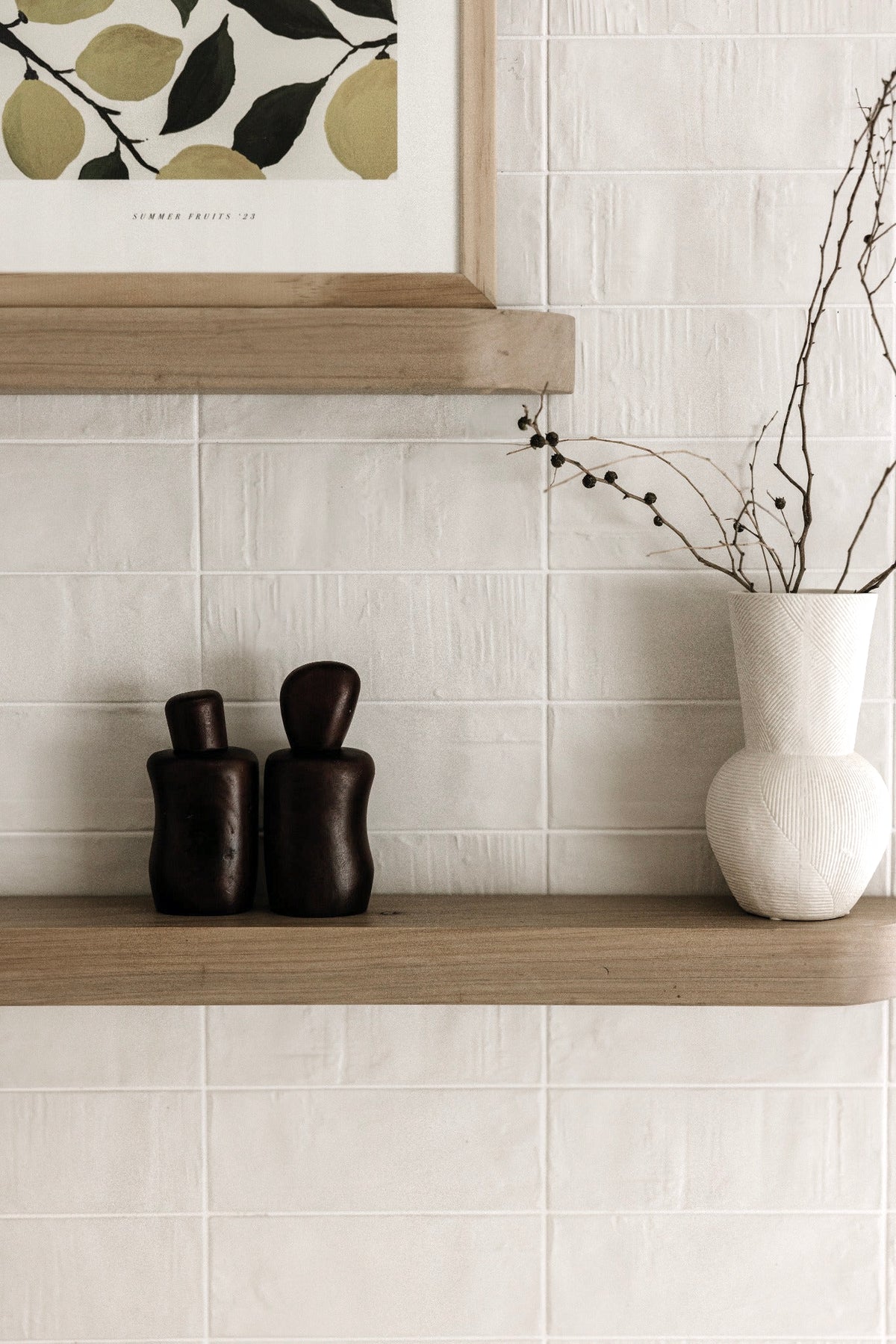 Dark brown wavy salt and pepper shakers on a wooden shelf with a white vase