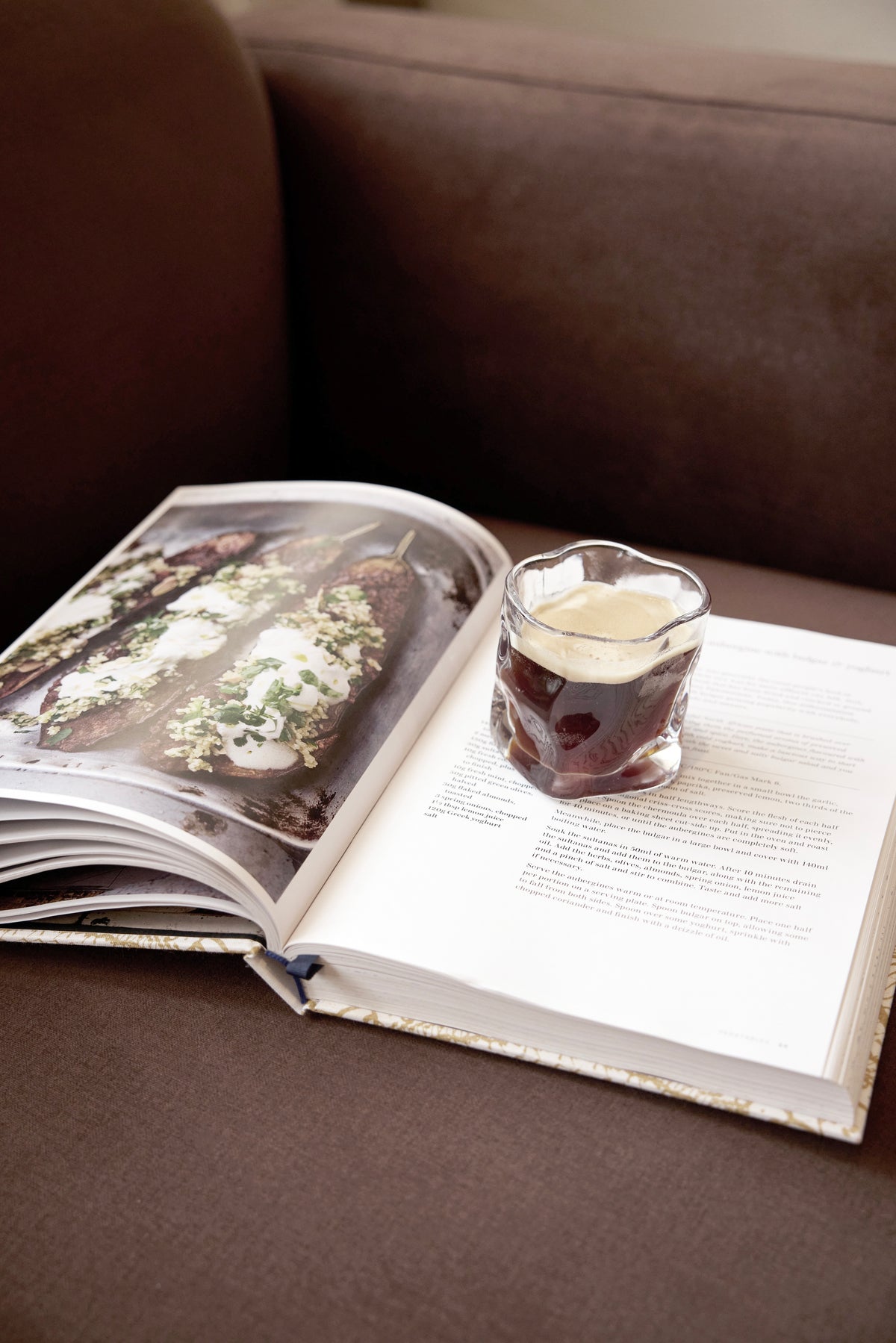 Wavy textured glass resting on an open recipe book on a brown sofa