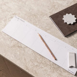 Weekly desk strip planner laid flat on stone desk with pencil in minimalist workspace