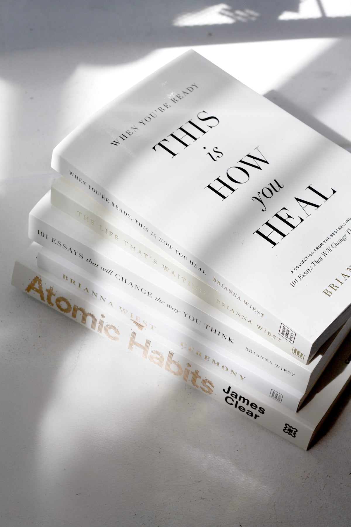 When You're Ready, This Is How You Heal on a stack of books in soft window light and shadow