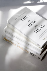 Brianna Wiest book collection including When You're Ready This Is How You Heal stacked with Atomic Habits by James Clear on a white surface with dramatic window light and shadows.