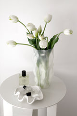 White faux tulip bouquet in a sculptural vase on a white side table, styled with perfume for a calm, minimal look