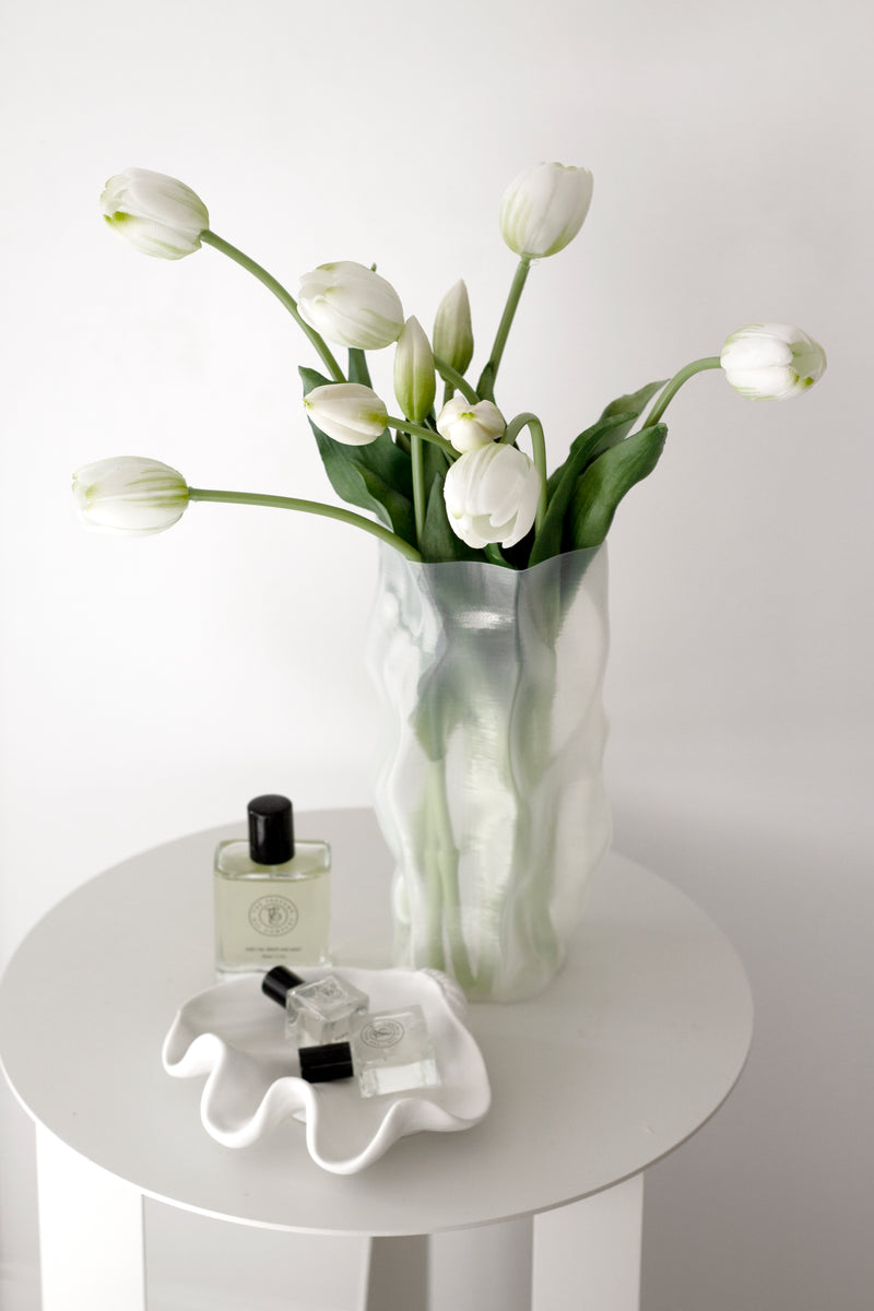 White faux tulip bouquet in a sculptural vase on a white side table, styled with perfume for a calm, minimal look