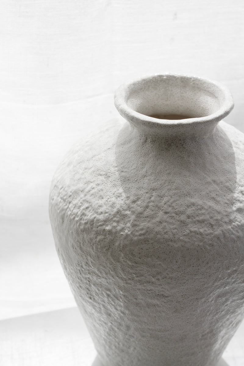 White textured vase photographed close-up by a window with soft lighting