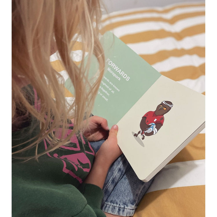 Child holding Wild About Footy open at an illustrated animal in a jersey