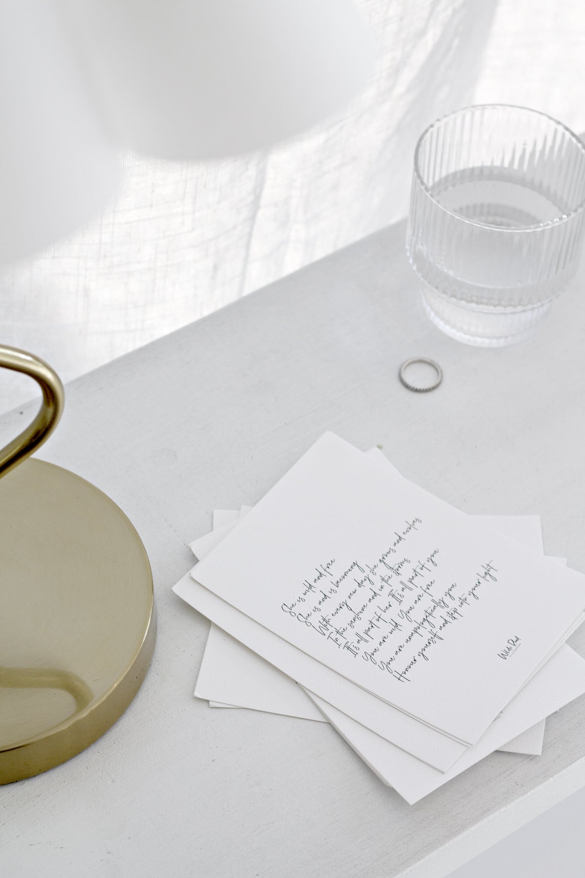 Minimal empowerment quote print cards styled on white bedside table with glass tumbler and brass lamp base