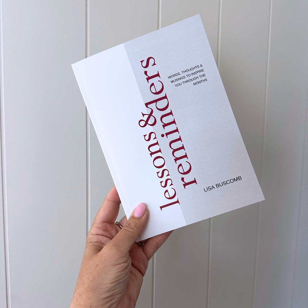 A hand holding a book titled 'Lessons & Reminders' by Lisa Buscomb.