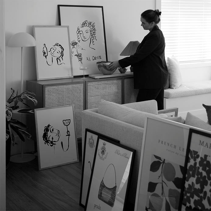 Black and white living room with the Wine All Day print leaning on a rattan sideboard among other framed prints
