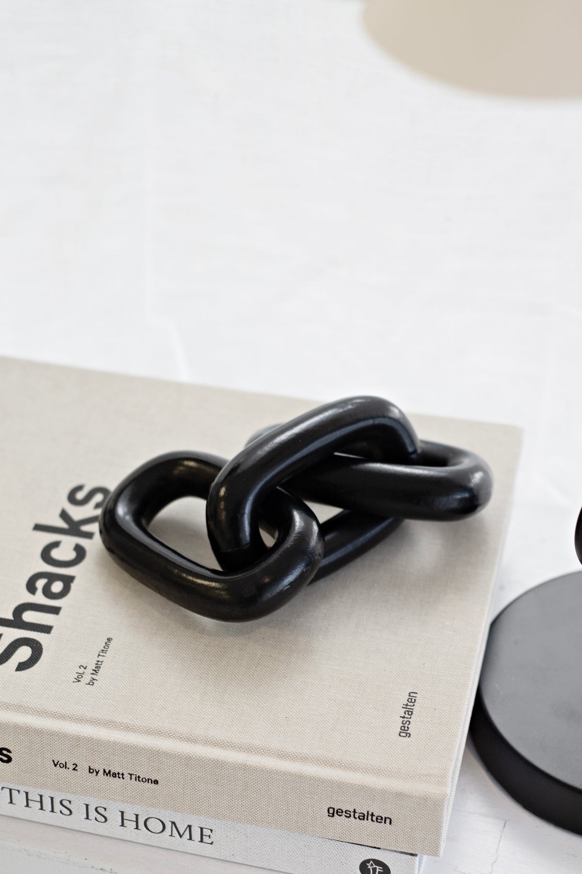 Black wooden chain ornament resting on a stack of neutral books beside a stone lid