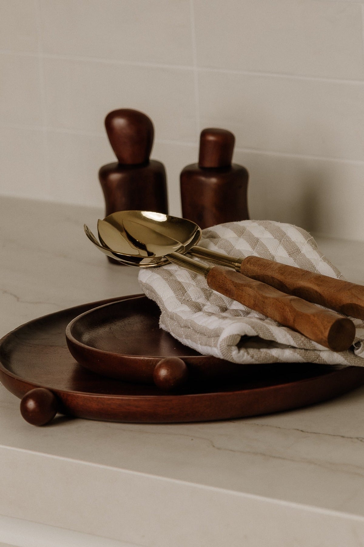 Dark brown wooden circle trays stacked on a stone bench with wooden shakers and linen napkins