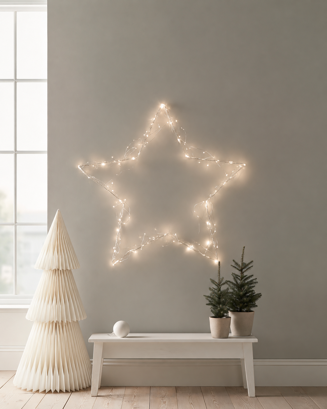 Papier HQ foldable paper Christmas tree in Scandi beige standing beside a white bench under a star of fairy lights