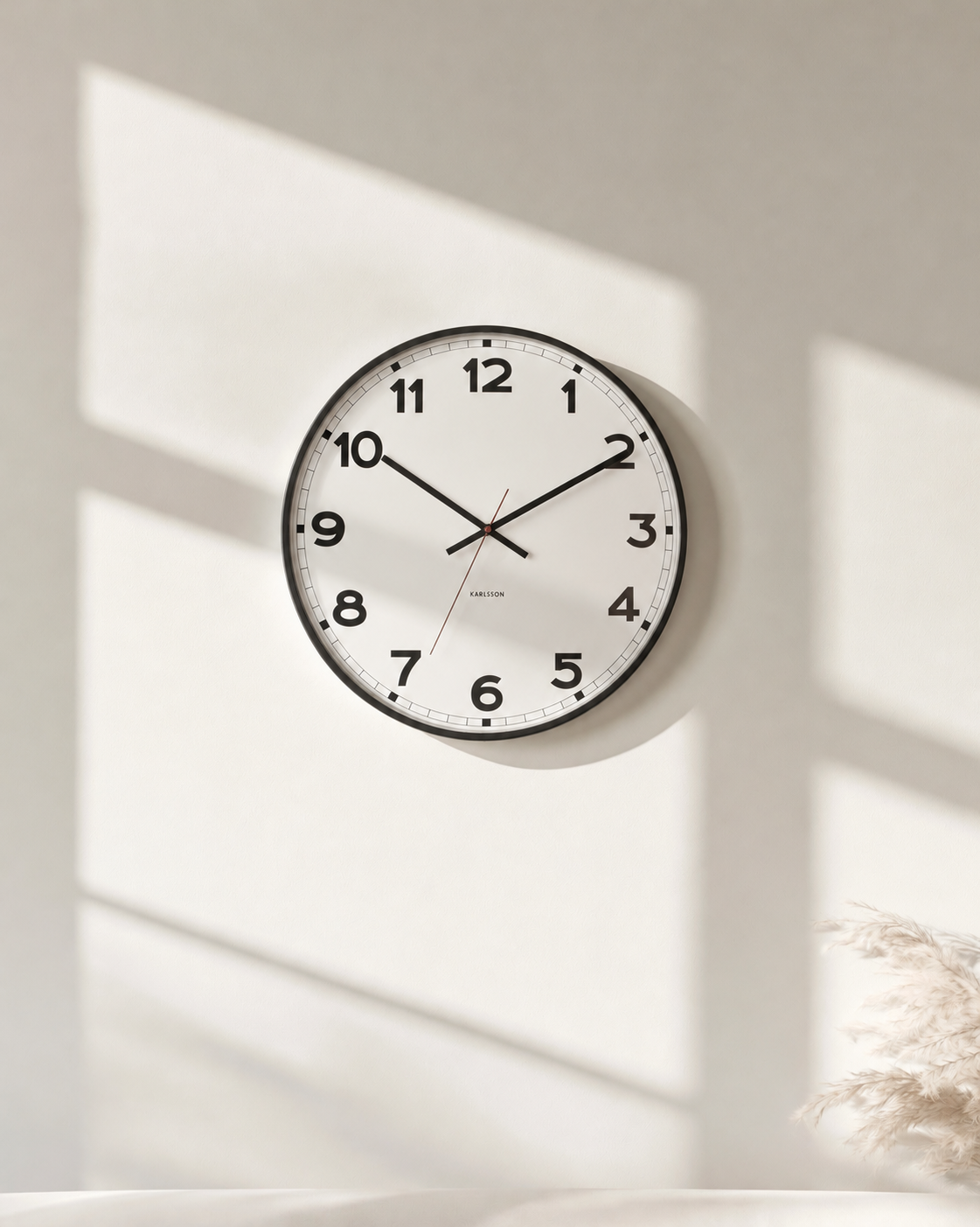Karlsson New Classic wall clock in white with black numerals on a sunlit plaster wall