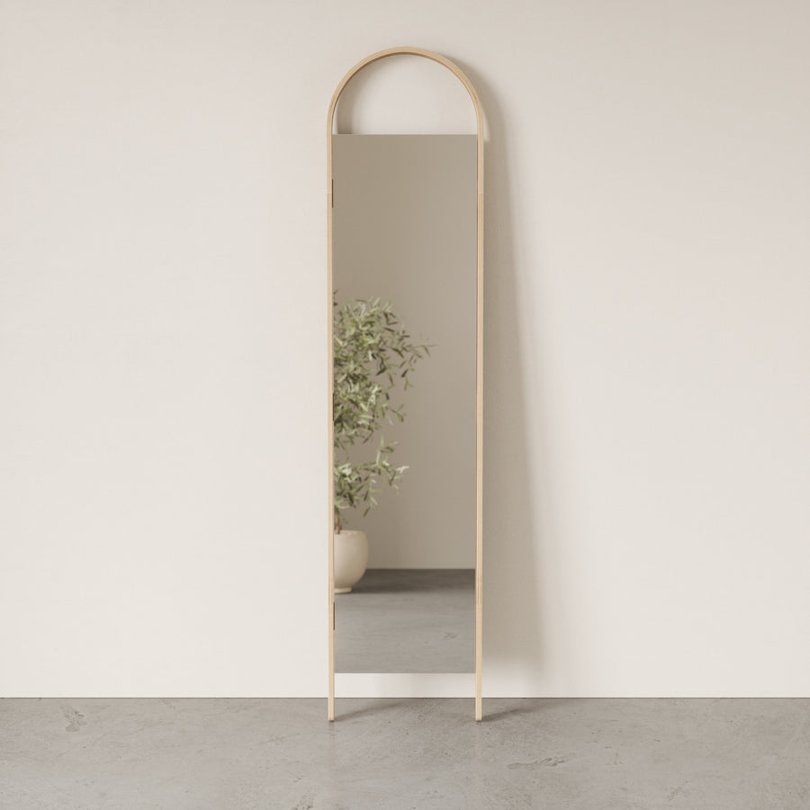 Umbra Bellwood leaning mirror in natural wood reflecting a plant in a bare room