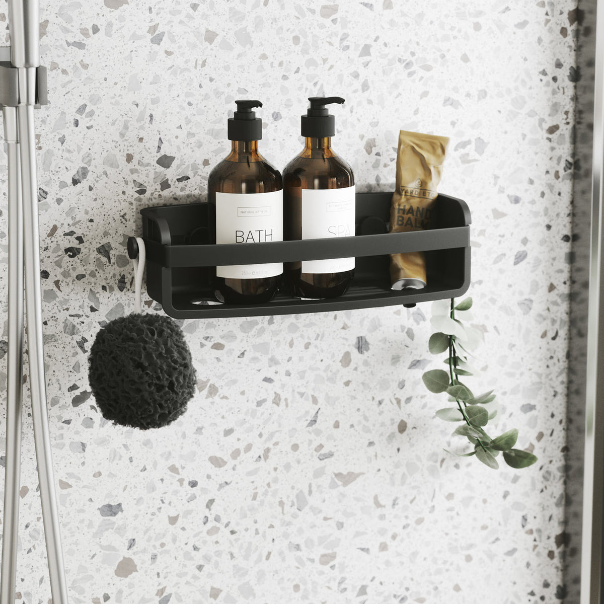 Umbra Flex adhesive shower bin in black on a terrazzo wall with bath bottles and a sponge
