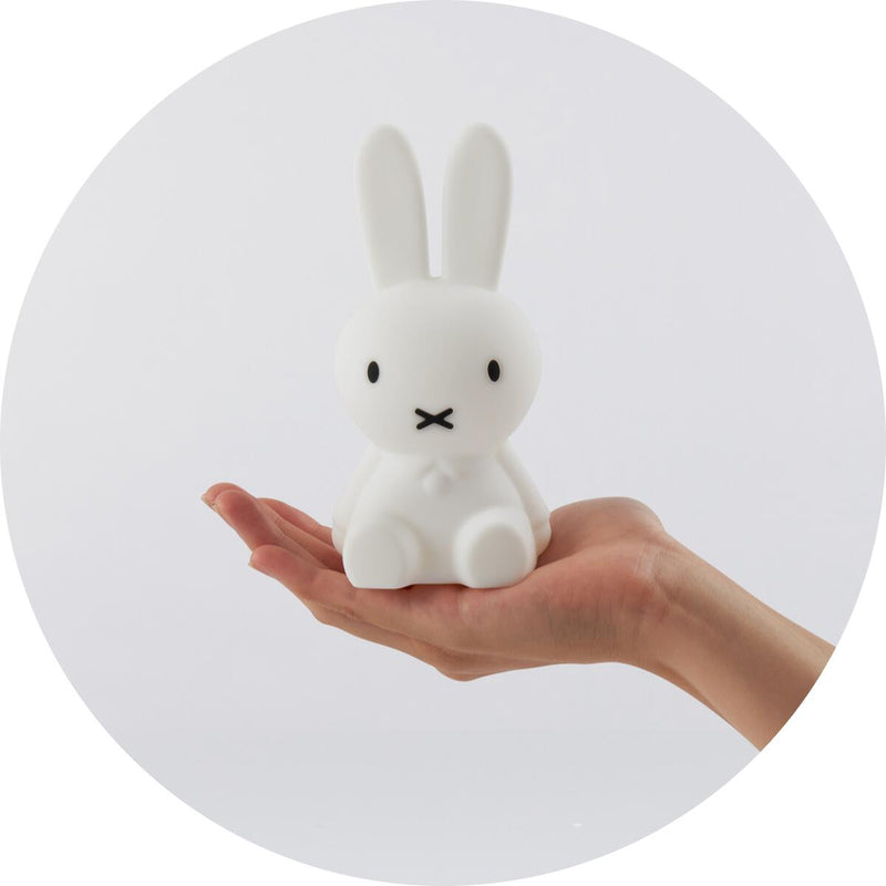 A person's hand holding a Miffy Bundle of Light, a small white bunny figurine by Mr Maria.