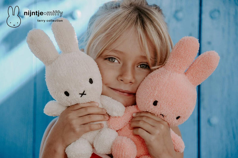 A little girl snuggling with two Mr Maria Miffy Sitting Terry Cream (23cm) plush rabbits.