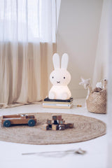 A medium-sized white bunny sitting on a rug next to a Mr Maria Miffy Star Light - DIMMABLE, MOOD LIGHTING.