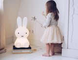 A little girl standing next to a Miffy Star Light - DIMMABLE, MOOD LIGHTING lamp, a medium-sized white bunny lamp with a unique design by Mr Maria.