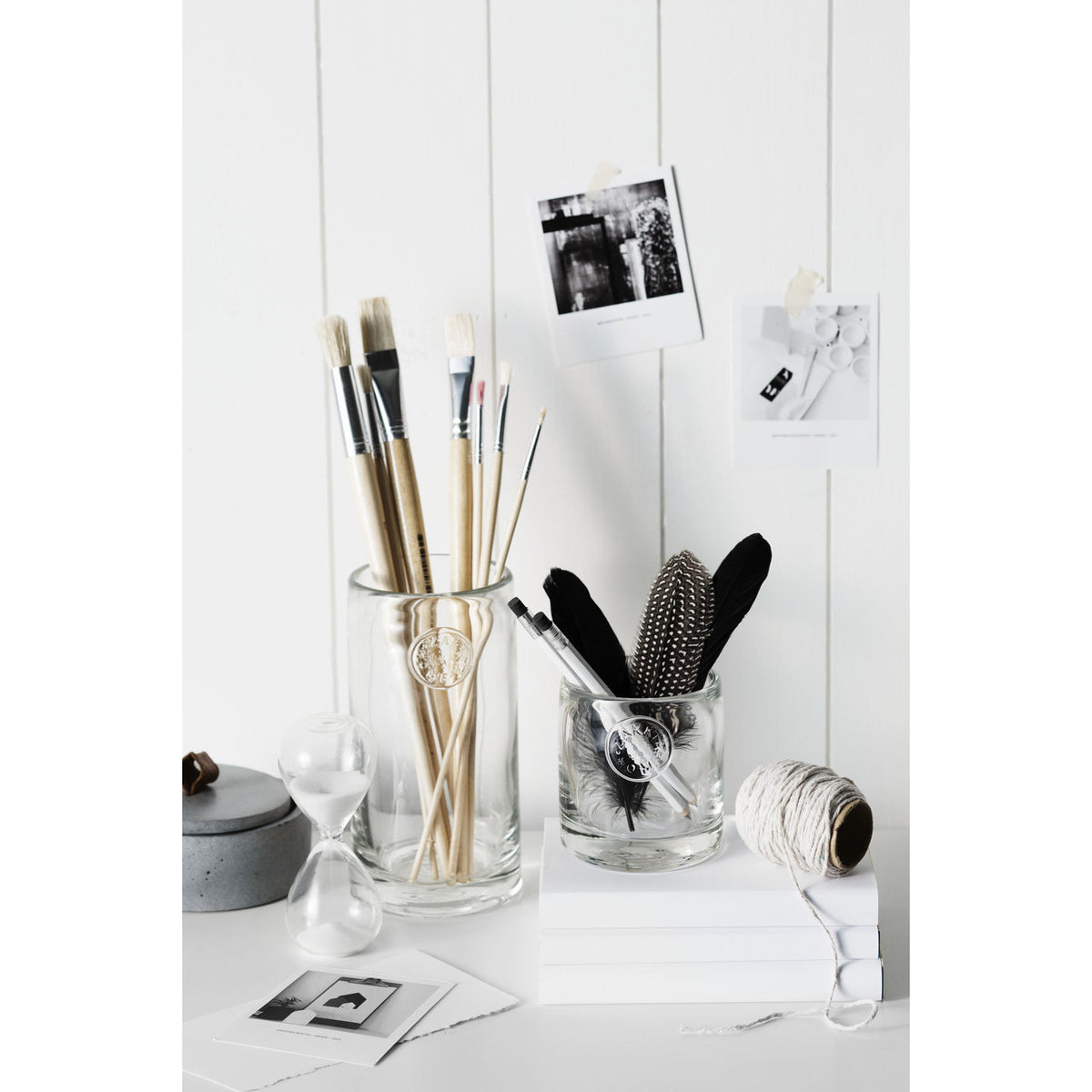 Hourglass standing on a desk beside glass jars of brushes and pens against white panelling