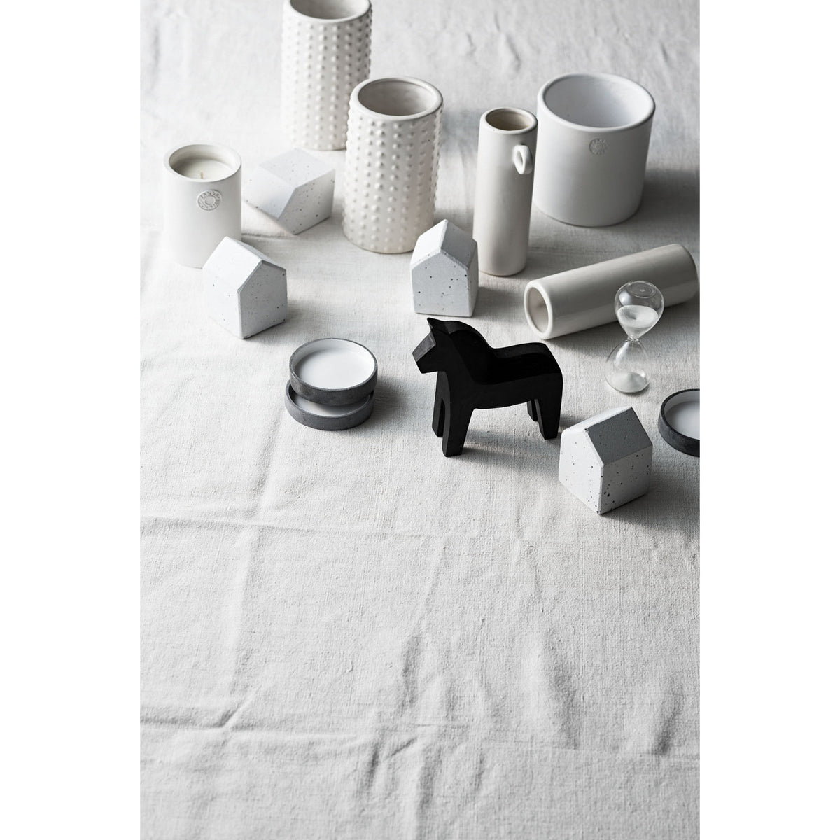 Small hourglass among white ceramic vessels and pots arranged on a linen cloth