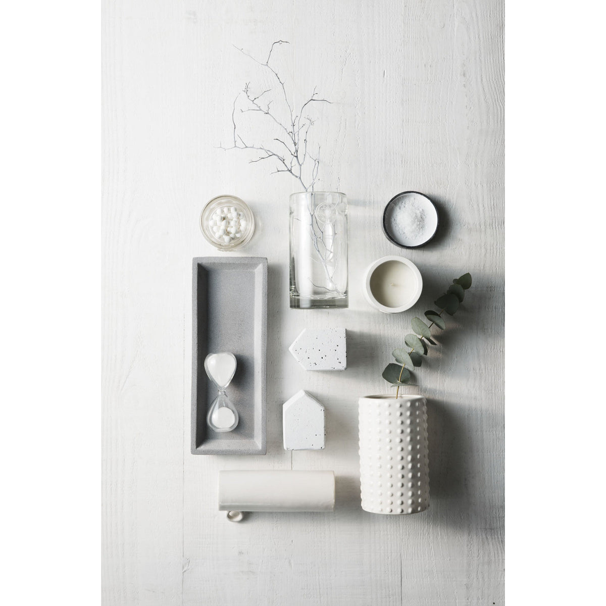 Hourglass lying in a concrete tray among pale ceramics and a branch, photographed from above
