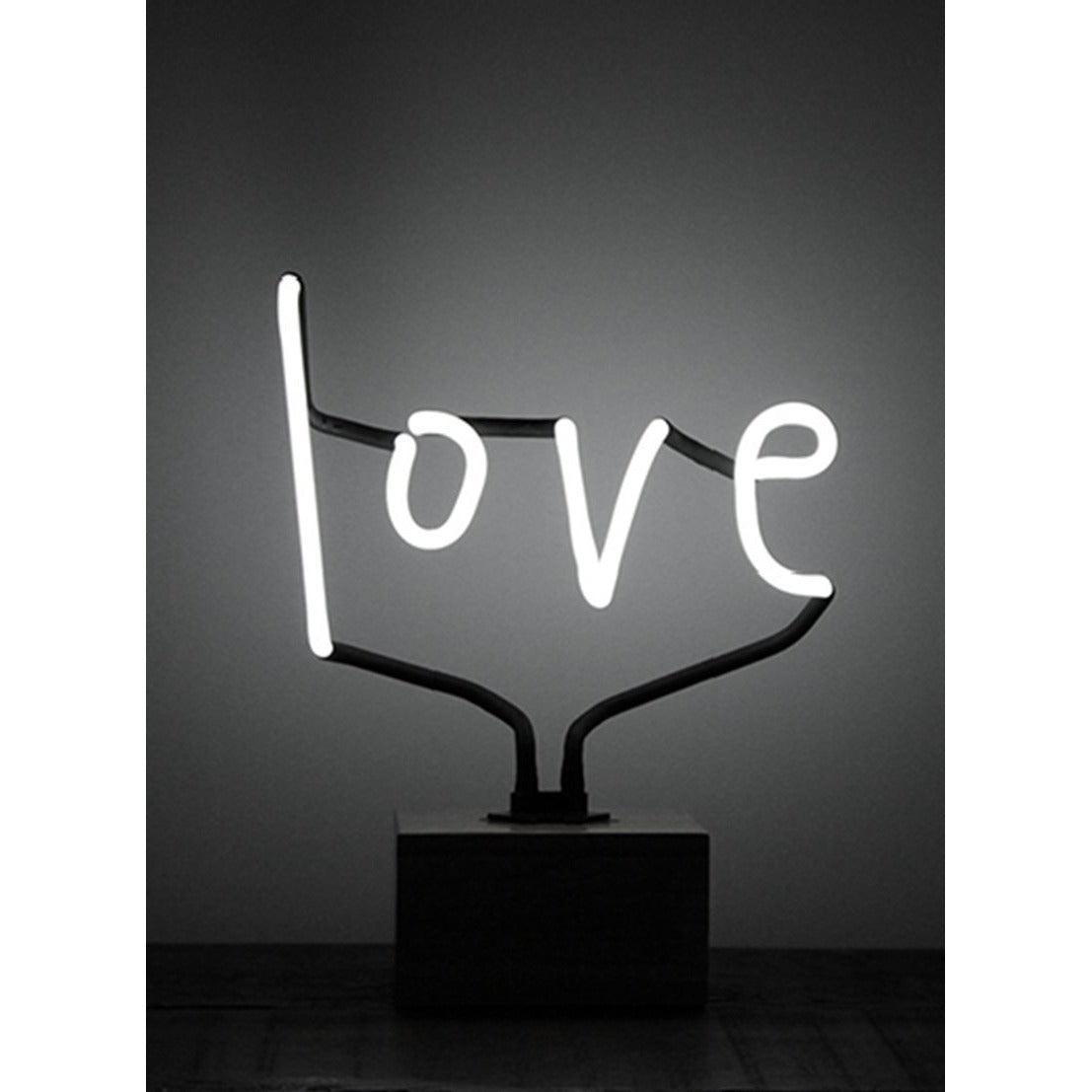 Love neon table lamp glowing white in cursive script on a black base