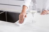 A woman using a Barkly Basics All White Cellulose Sponge - Pack of 3 to wipe a glass of wine on a kitchen counter.