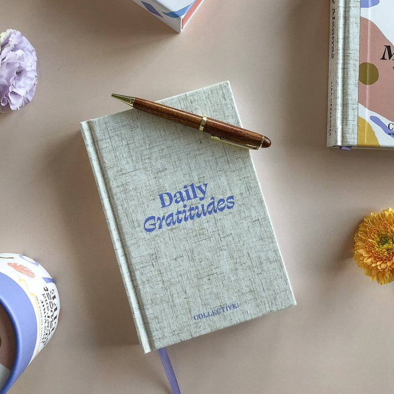 A Daily Gratitudes Version 2 journal adorned with beautiful flowers, accompanied by a Collective Hub pen for expressing gratitude.