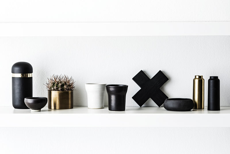 A black shelf with Zakkia Concrete Cross Trivet - Black and gold vases and a cactus.