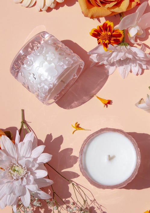 Two Fleur D'Oranger candles on a peach backdrop, one tipped on its side among autumn blooms