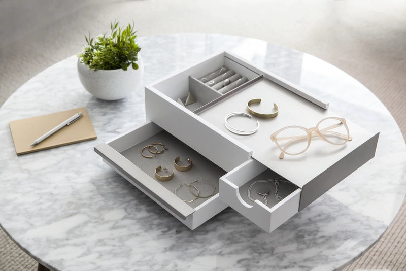 A white Umbra Stowit Jewelry Box WHT/NKL with glasses, a pen, and a notebook atop a table.